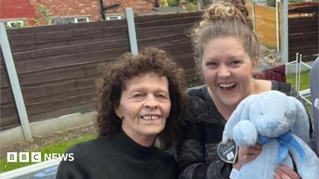 An older woman, two young women and a young man stand smiling at the camera as the young woman on the right takes a "selfie". The other young woman is holding a blue stuffed rabbit.